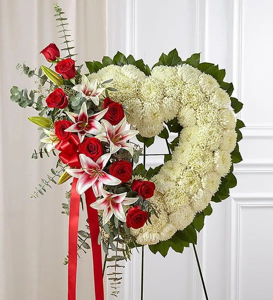 Heart-shaped white wreath with red roses and white lilies on a standing easel