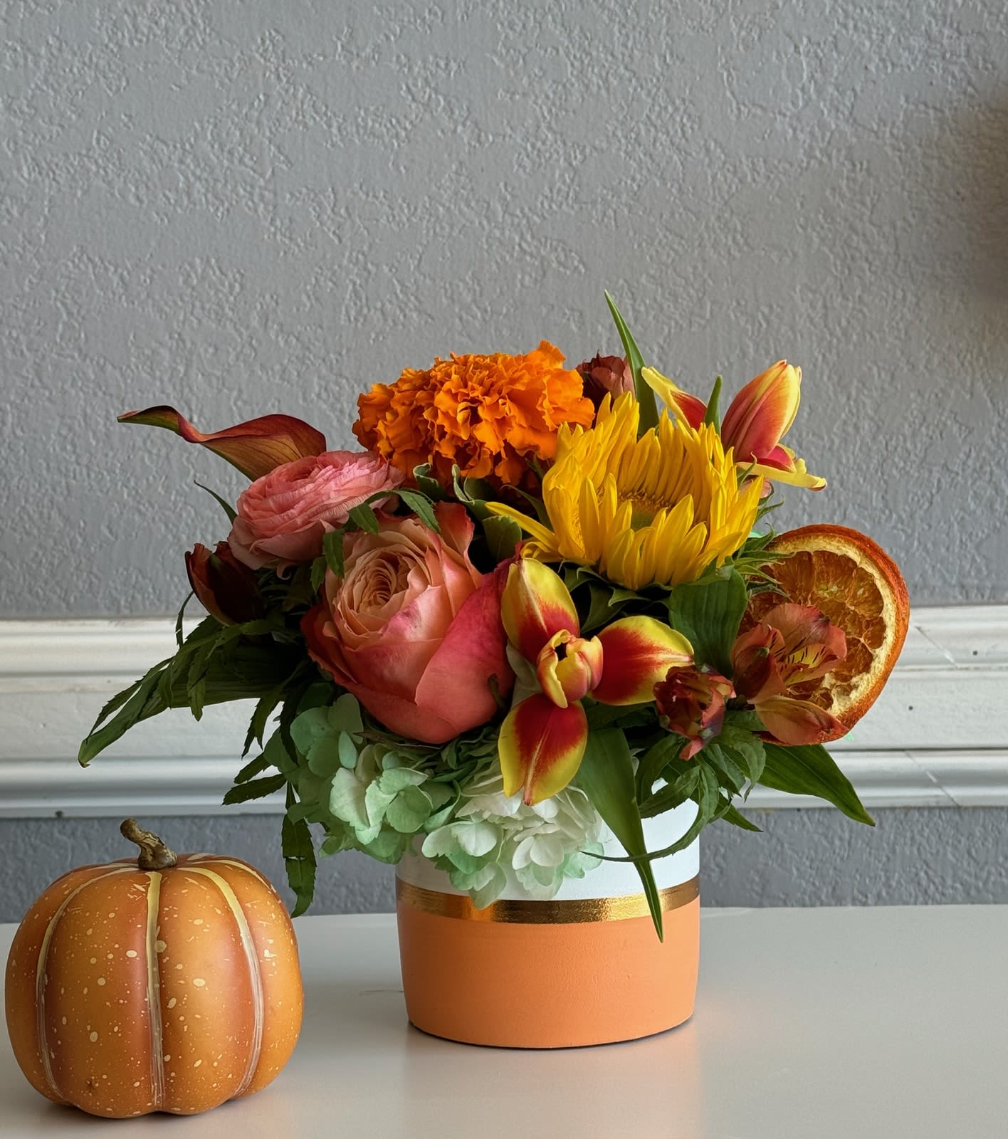 Autumn bouquet in a peach vase with a small decorative pumpkin beside it.