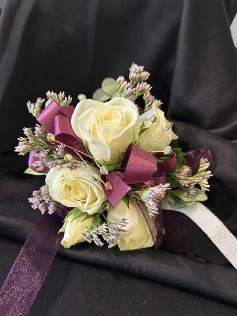 Small bouquet of cream roses with purple ribbon on black fabric