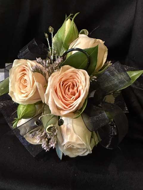 Peach roses arranged with black ribbon on a dark background