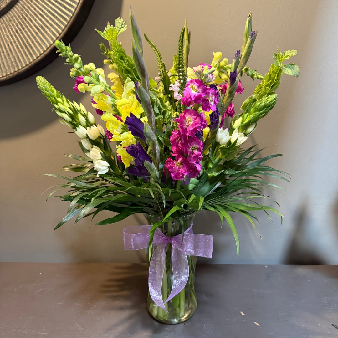 Colorful bouquet of snapdragons and iris in a glass vase with a purple ribbon