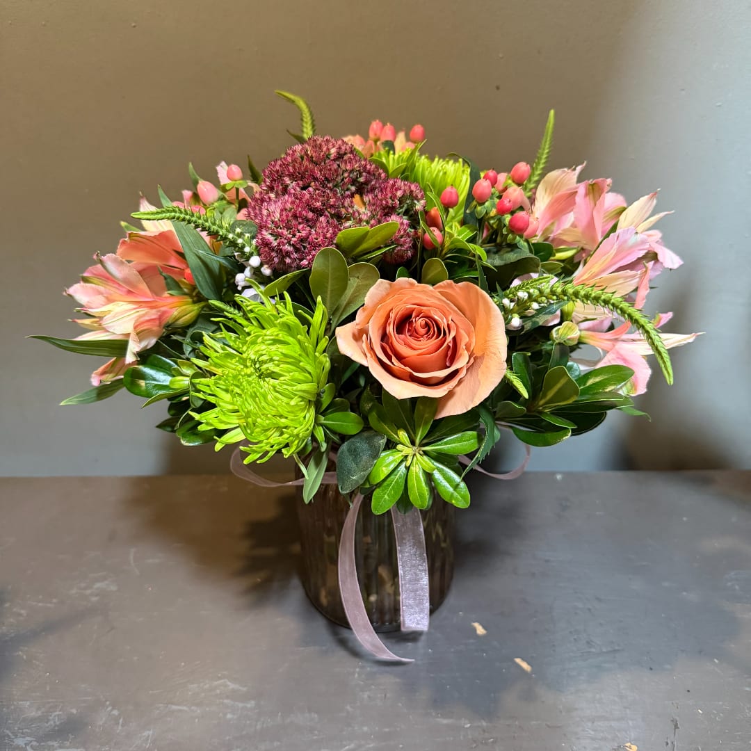 Mixed bouquet in a dark glass vase with peach and pink blooms