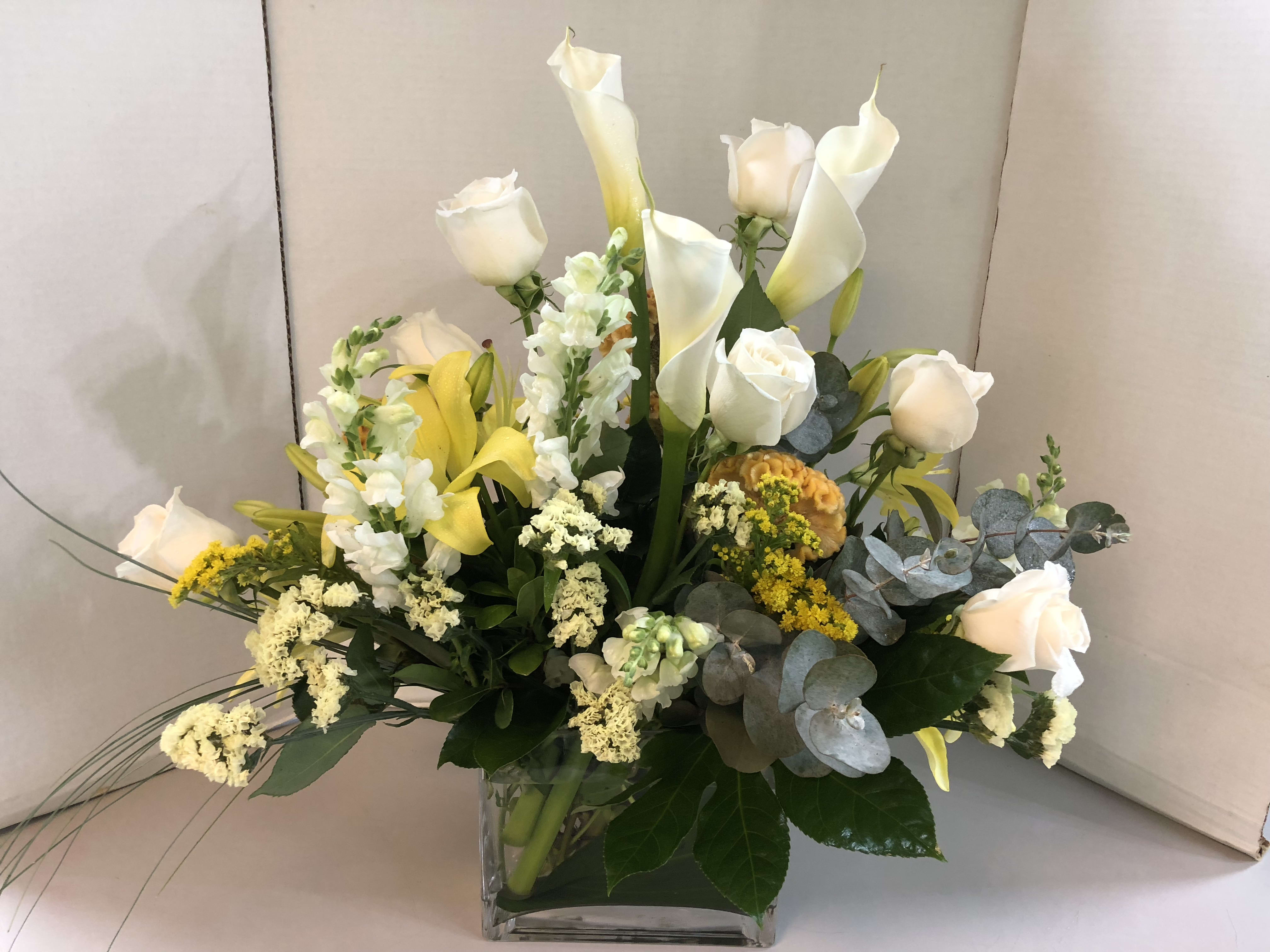 White roses and calla lilies arranged in a clear square vase