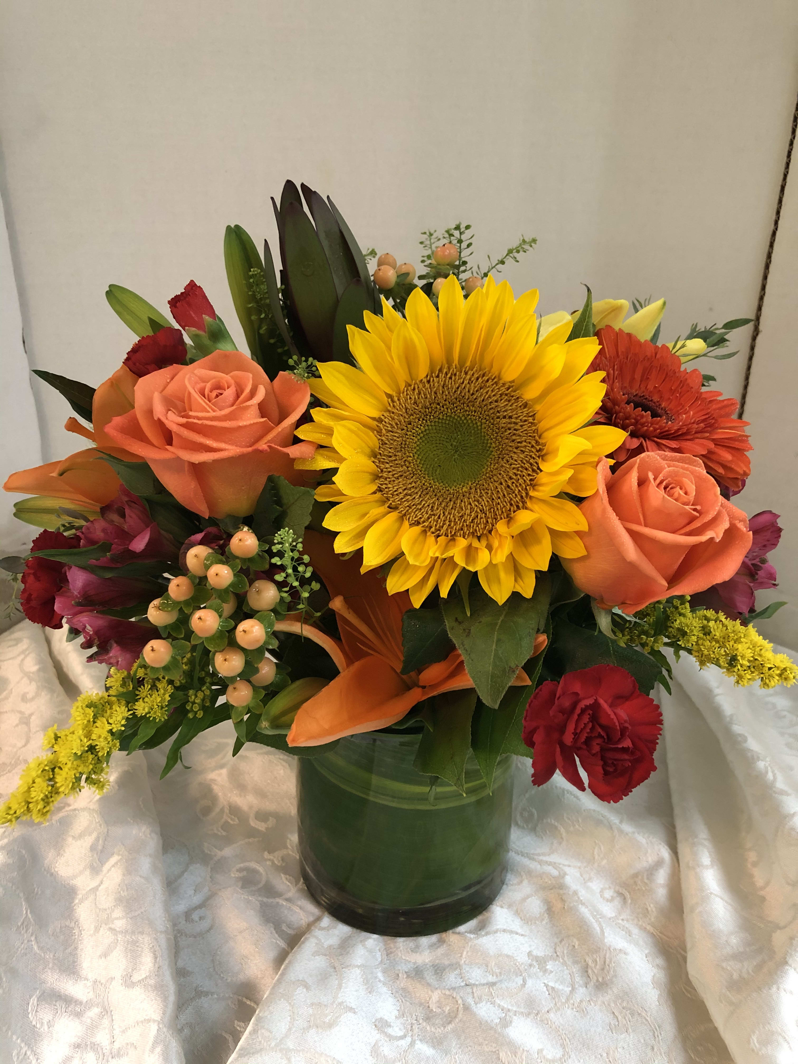 Mixed bouquet with sunflowers, orange roses, and red flowers in a green vase