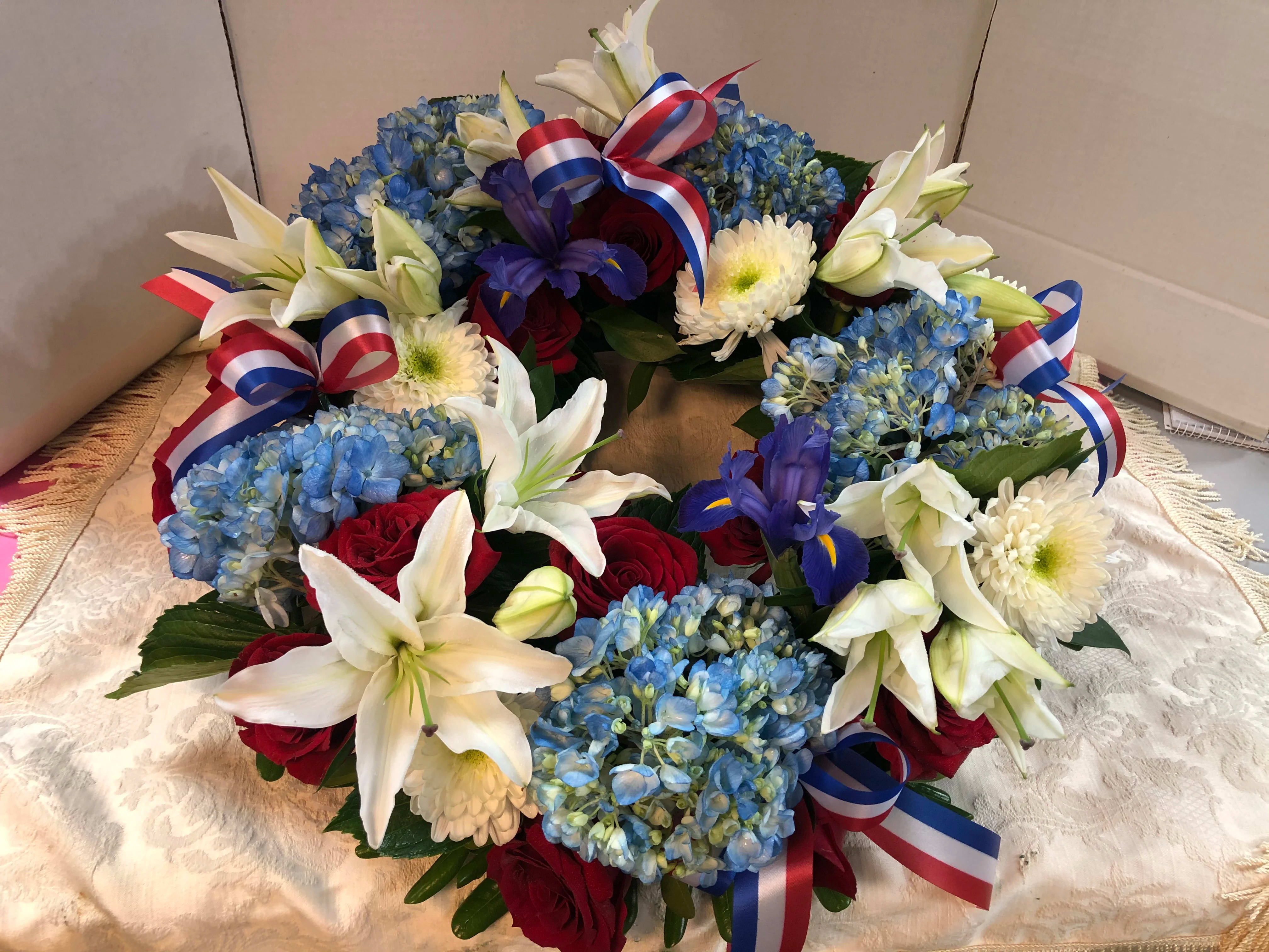 Floral wreath with blue hydrangeas, white lilies, red roses, and ribbon bows
