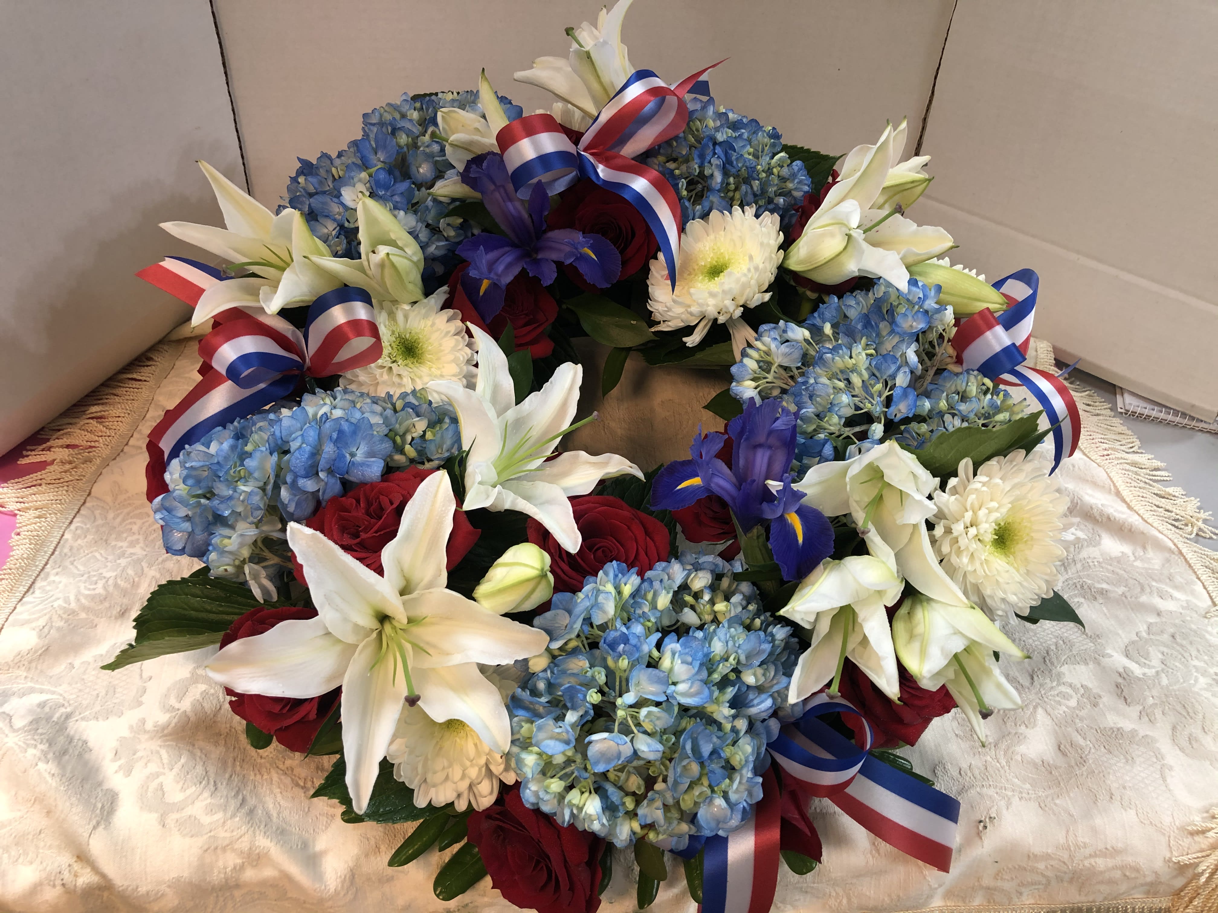 Wreath of blue hydrangeas, white lilies, red roses, and ribbon bows