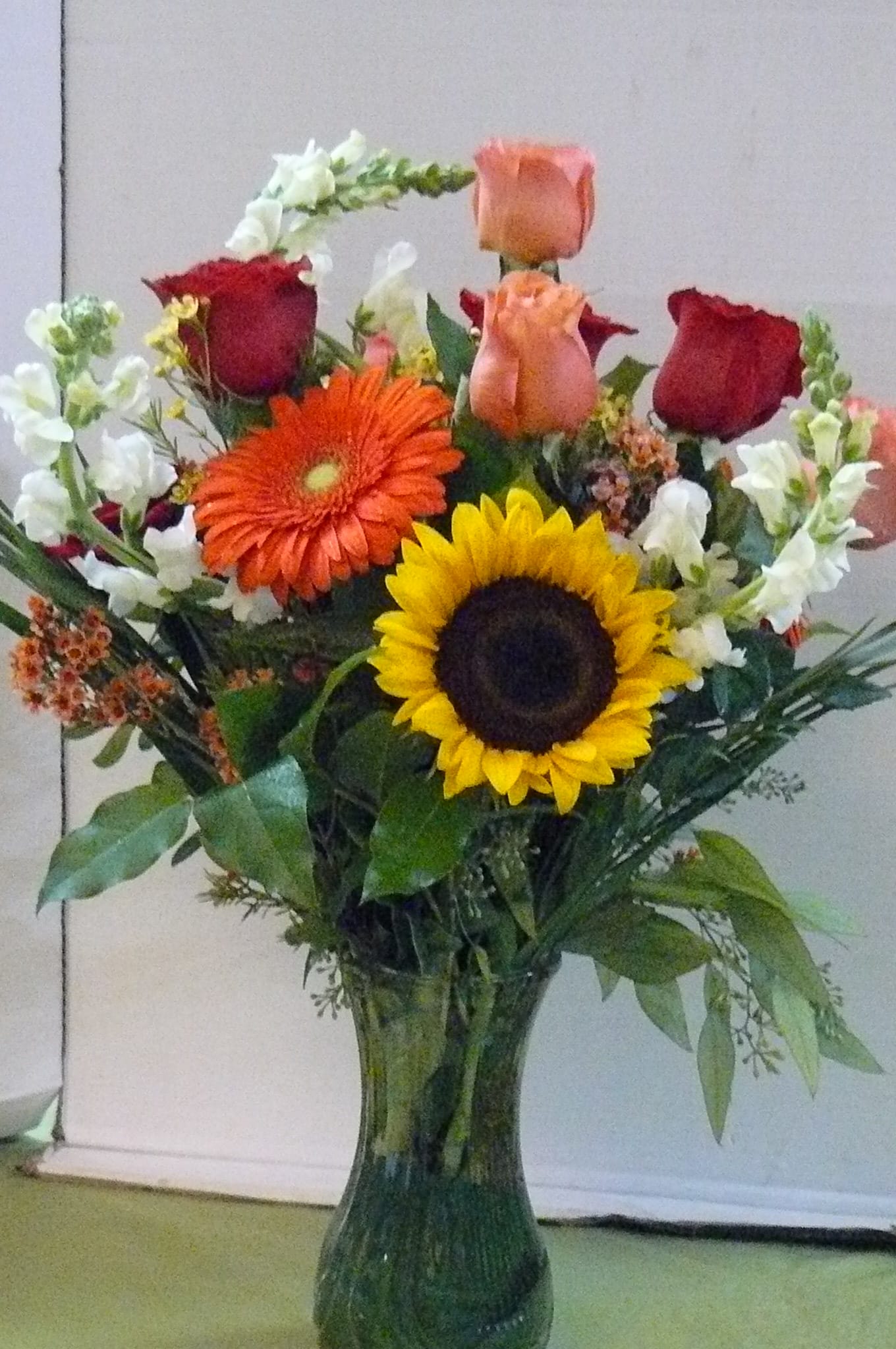 Mixed bouquet of roses, gerbera daisies, and sunflowers in a glass vase