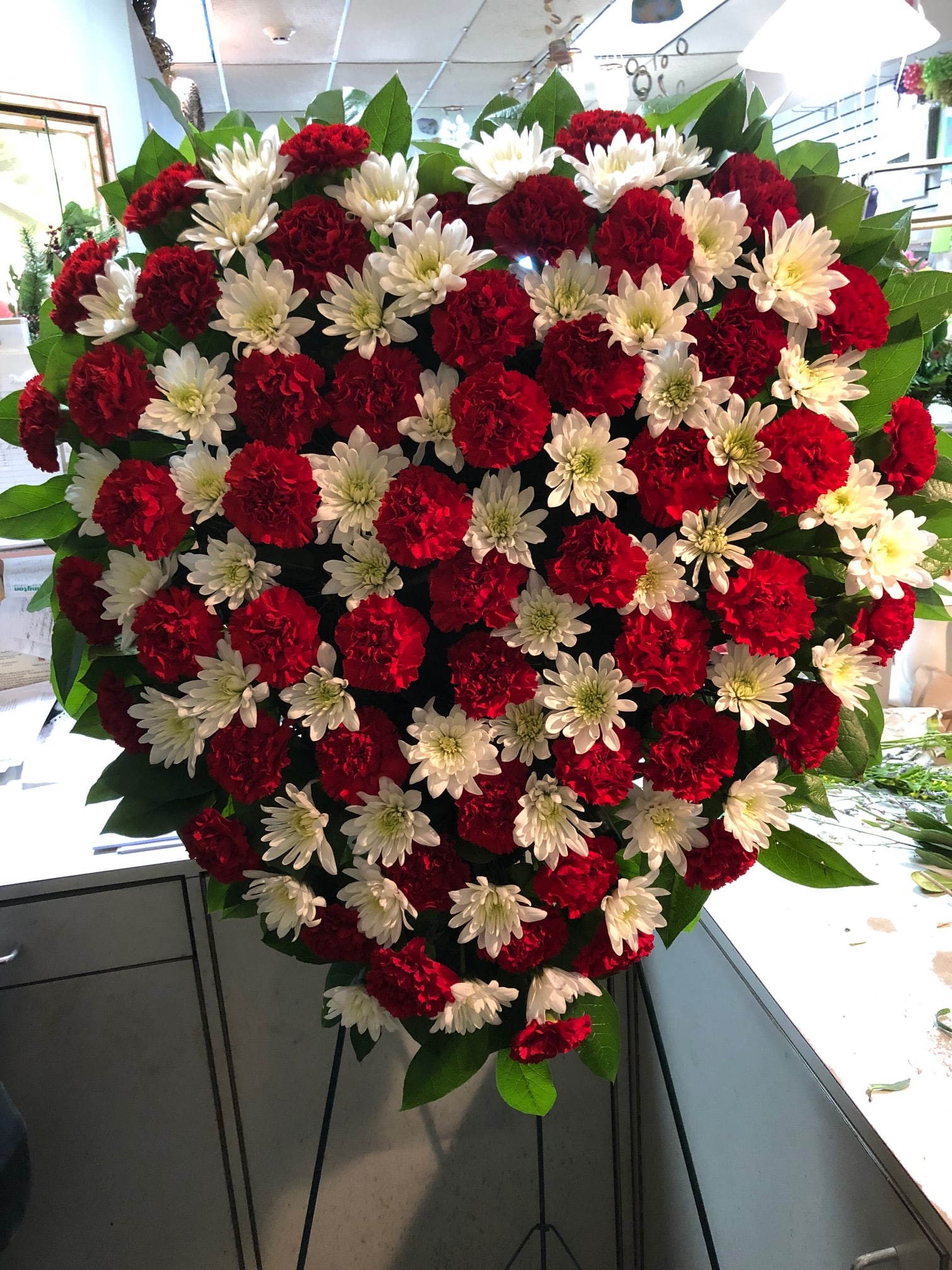 Heart-shaped floral spray of red carnations and white daisies on a stand