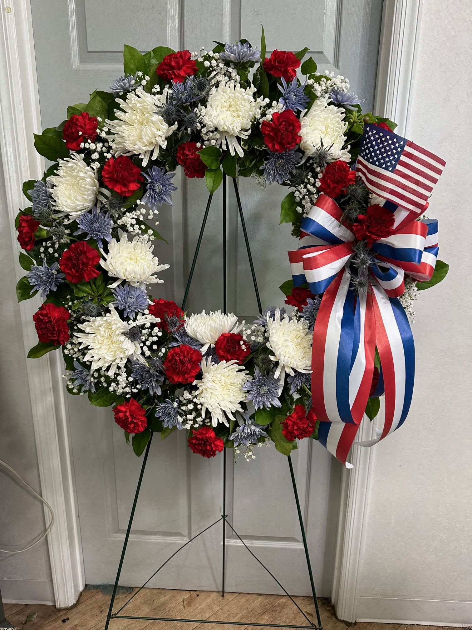 Red, white, and blue floral wreath on a stand with an American flag ribbon