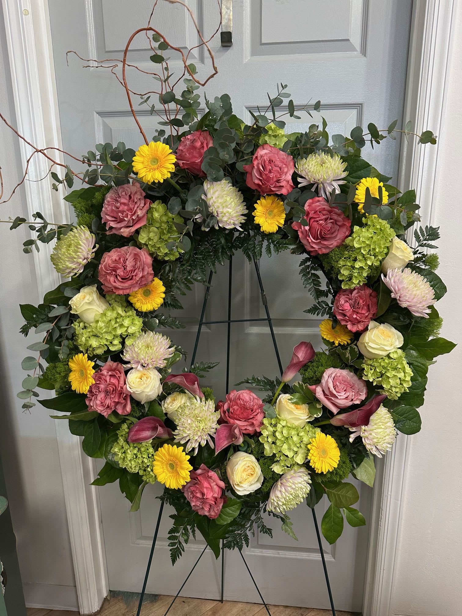Large floral wreath with pink roses, yellow daisies, and green hydrangeas on an easel