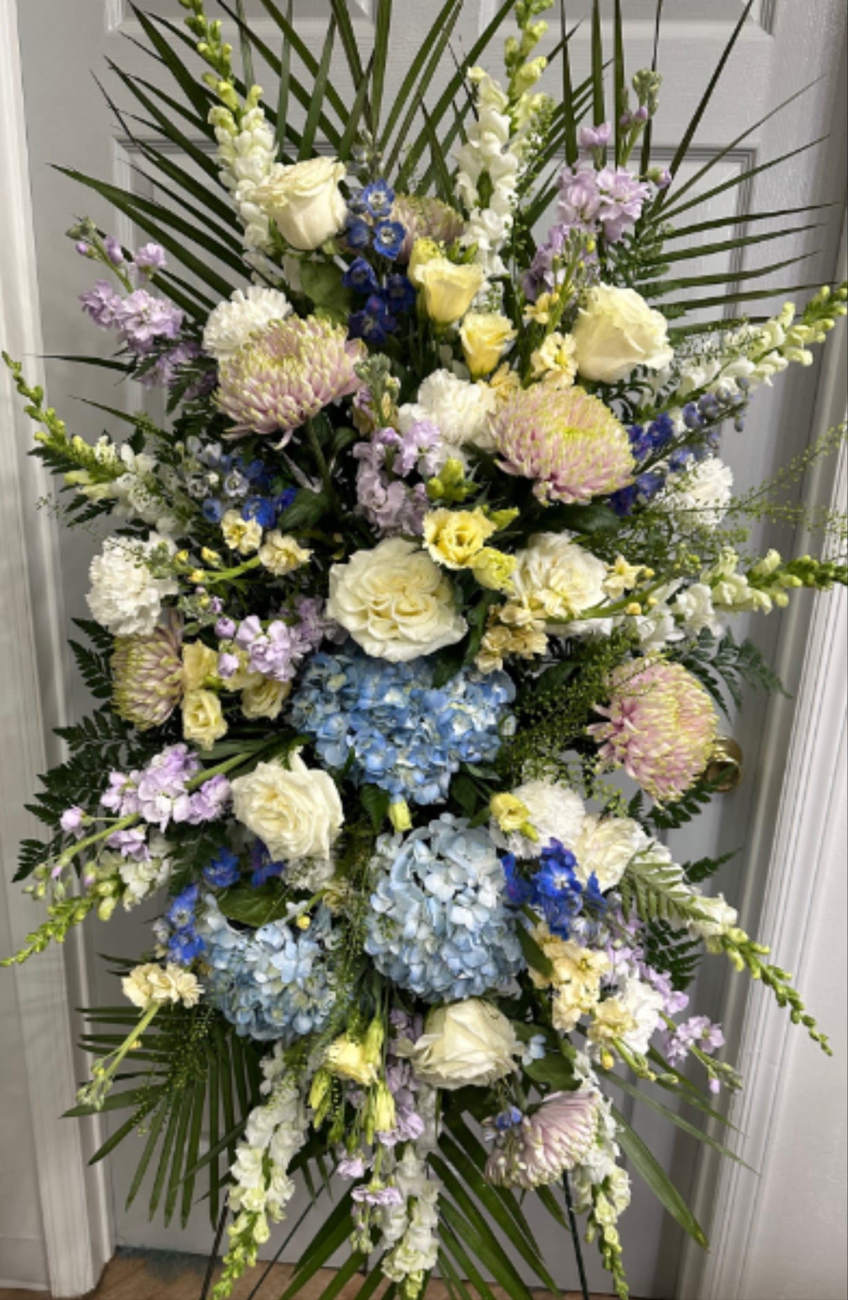 Tall standing floral spray with blue hydrangeas, white roses, and pastel blooms