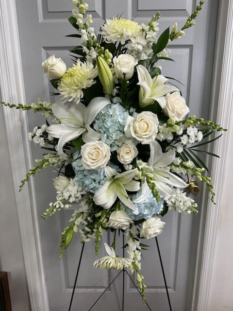 White floral standing spray with lilies, roses, and blue hydrangeas on an easel