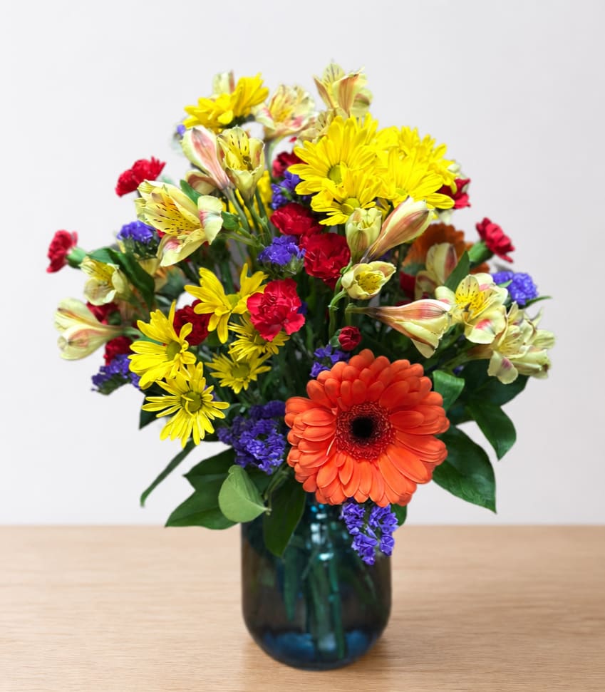 Mixed bouquet in a blue glass vase with orange, yellow, red, and purple flowers