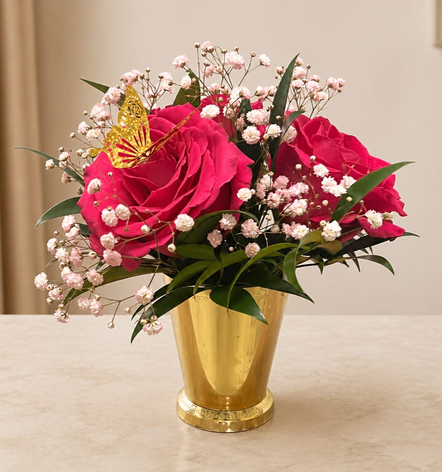 Pink roses in a gold vase with baby's breath and a butterfly accent