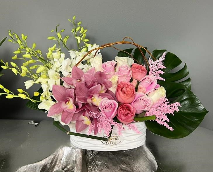 Pink roses and orchids arranged in a white basket with large green leaves