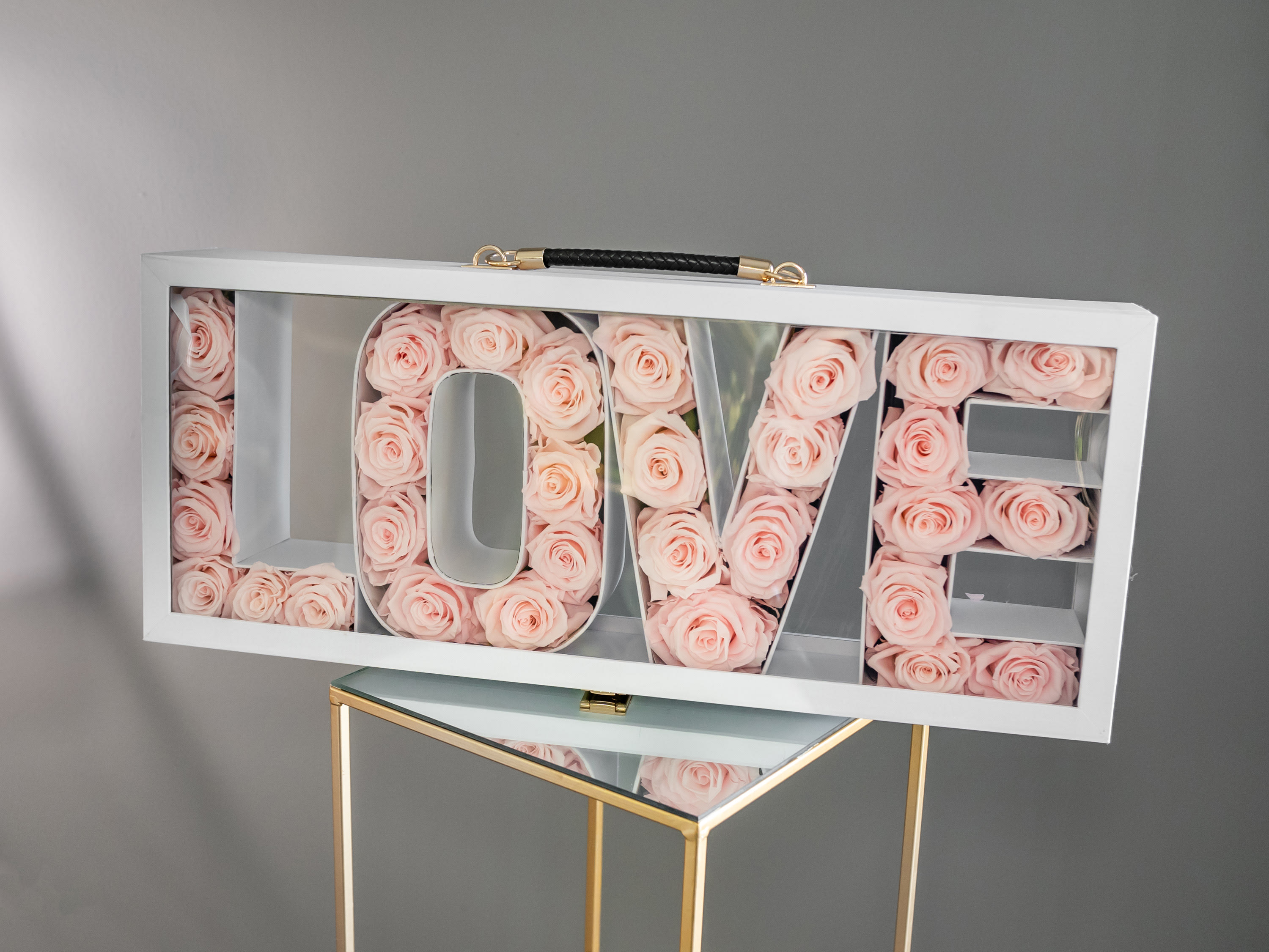White box sign spelling LOVE filled with pale pink roses