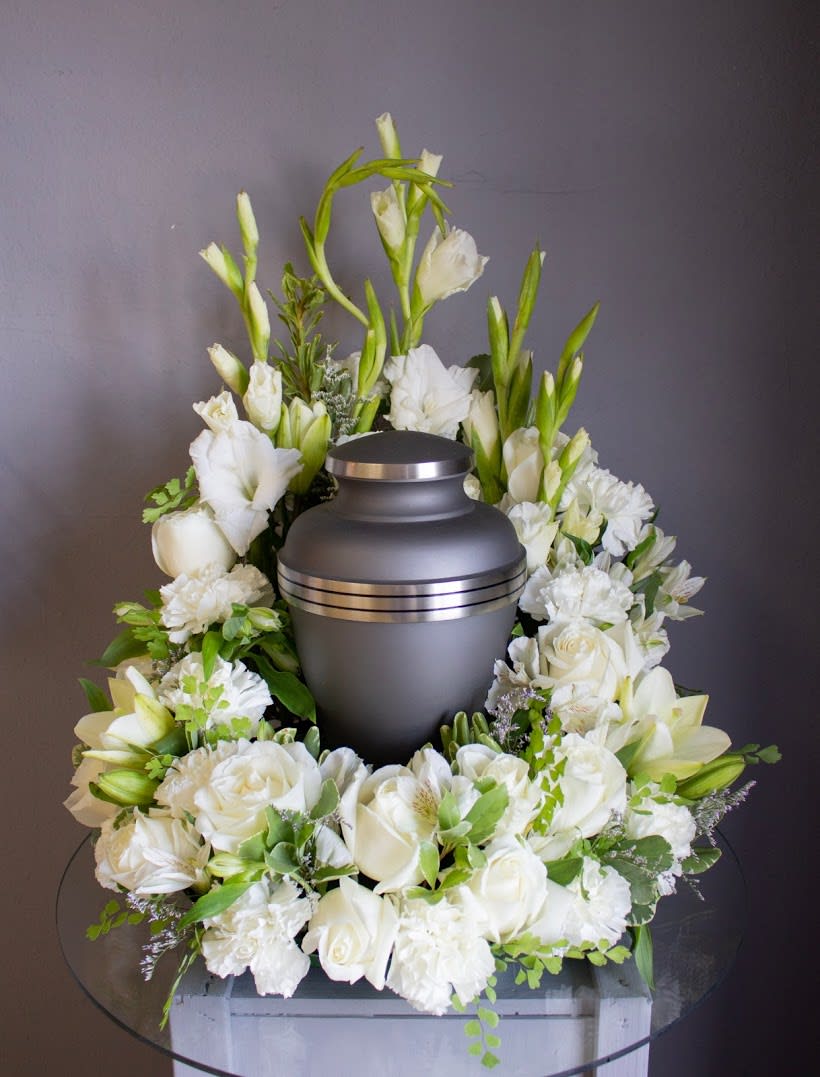 Cremation urn encircled by white roses, lilies, and carnations in a wreath-style arrangement