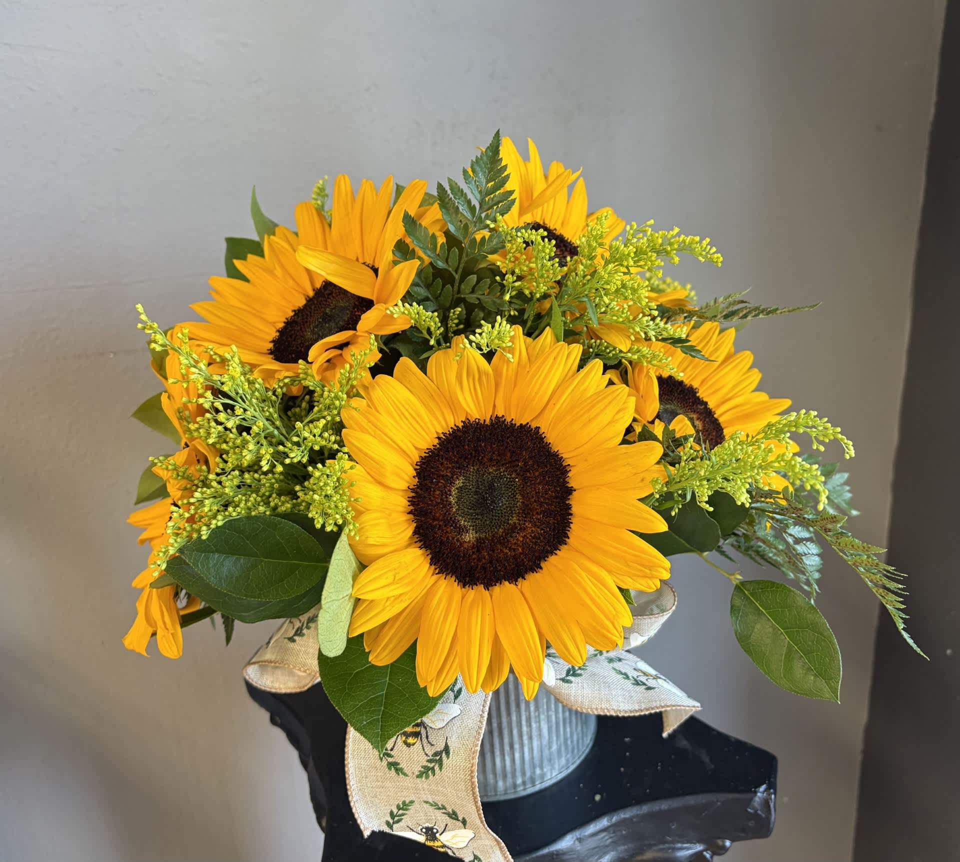 Bouquet of yellow sunflowers in a ribbed metal container with a ribbon