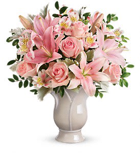 Pink lilies, roses, and alstroemeria arranged in a pale ceramic vase