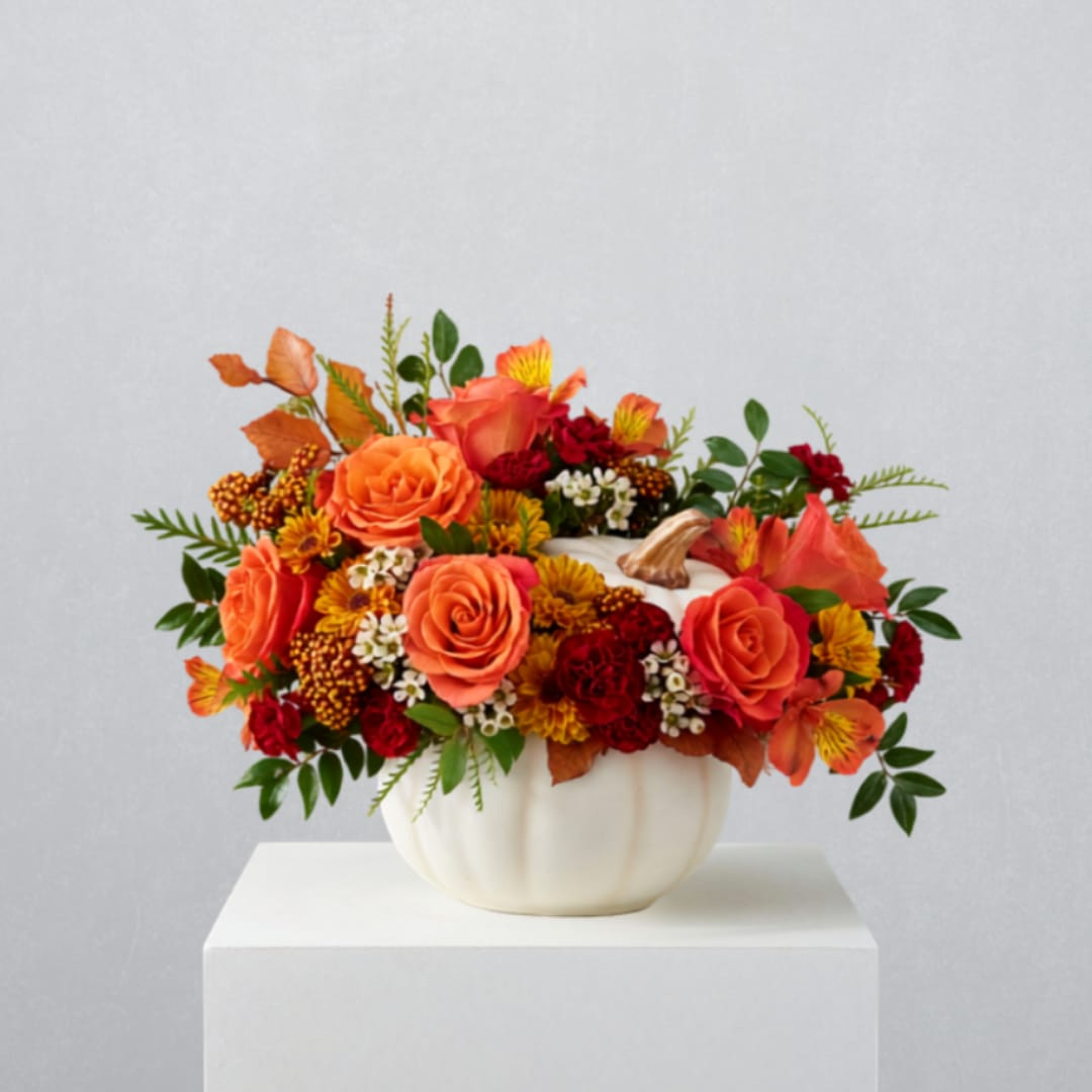 Orange and red floral arrangement in a white pumpkin vase