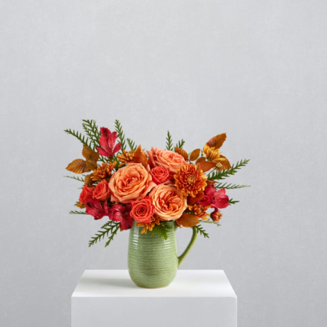 Orange and red flower arrangement in a green pitcher vase