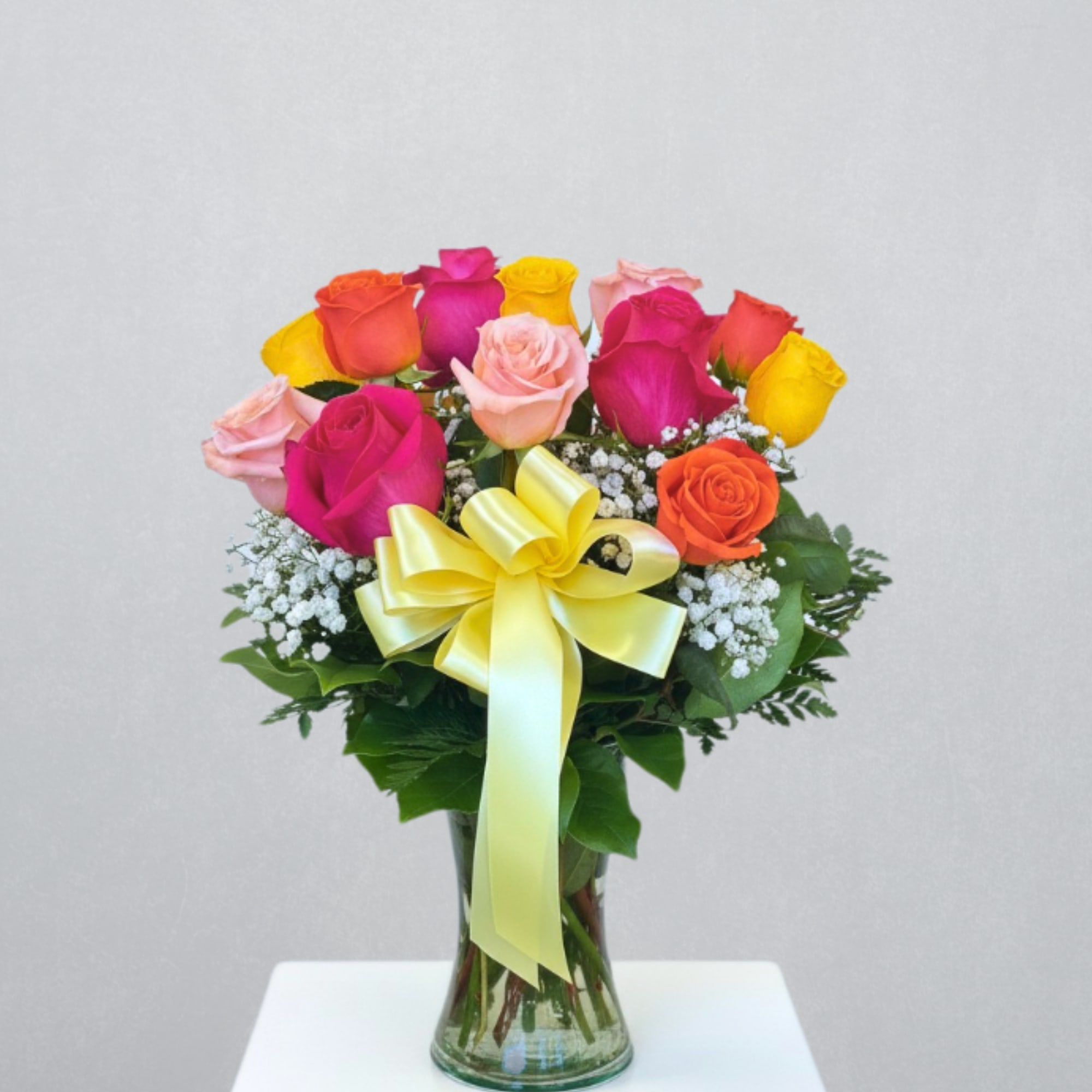 Bright mixed-color rose arrangement with baby's breath in a glass vase with a yellow bow