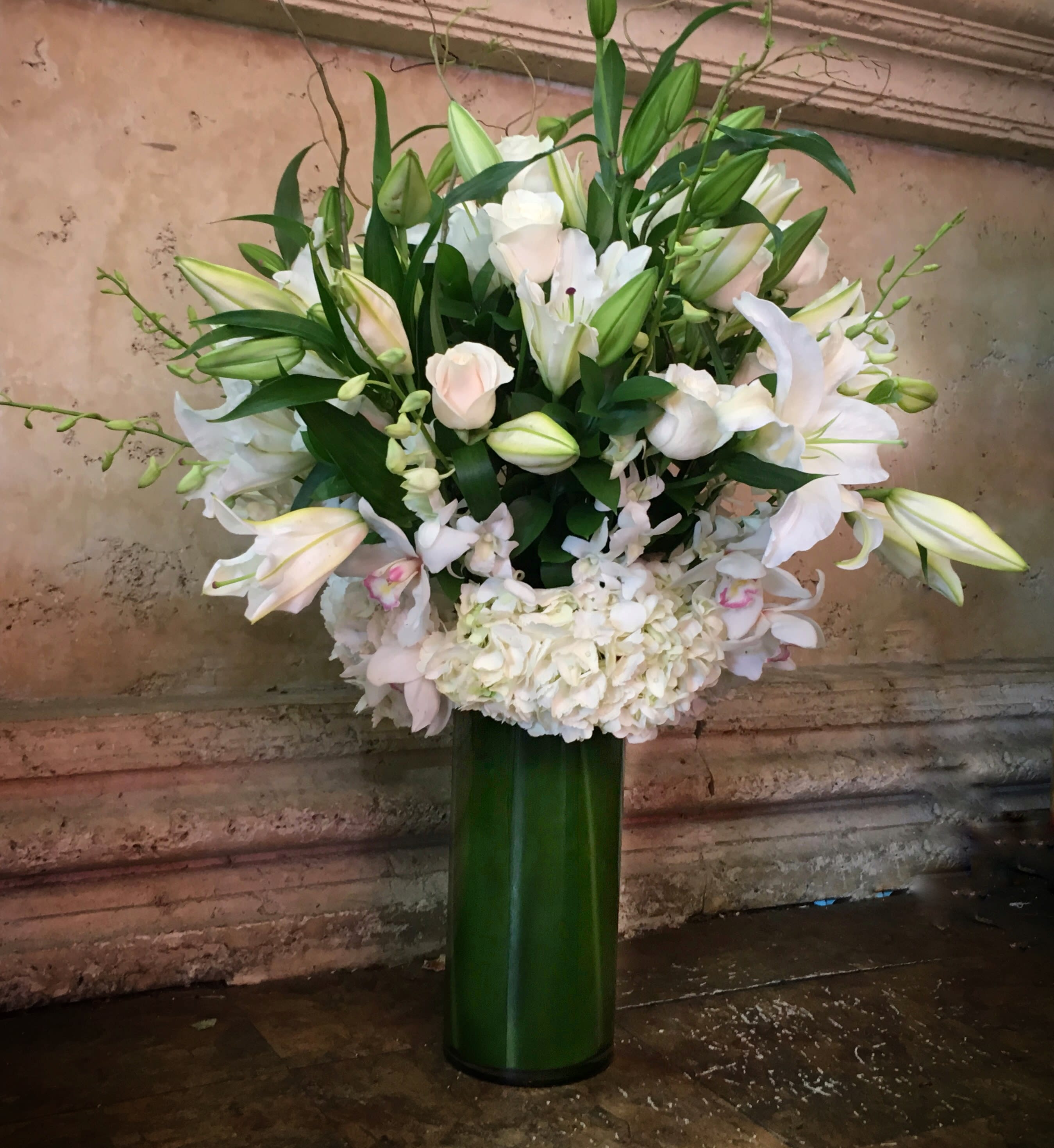 White lilies and pale pink roses in a tall green vase