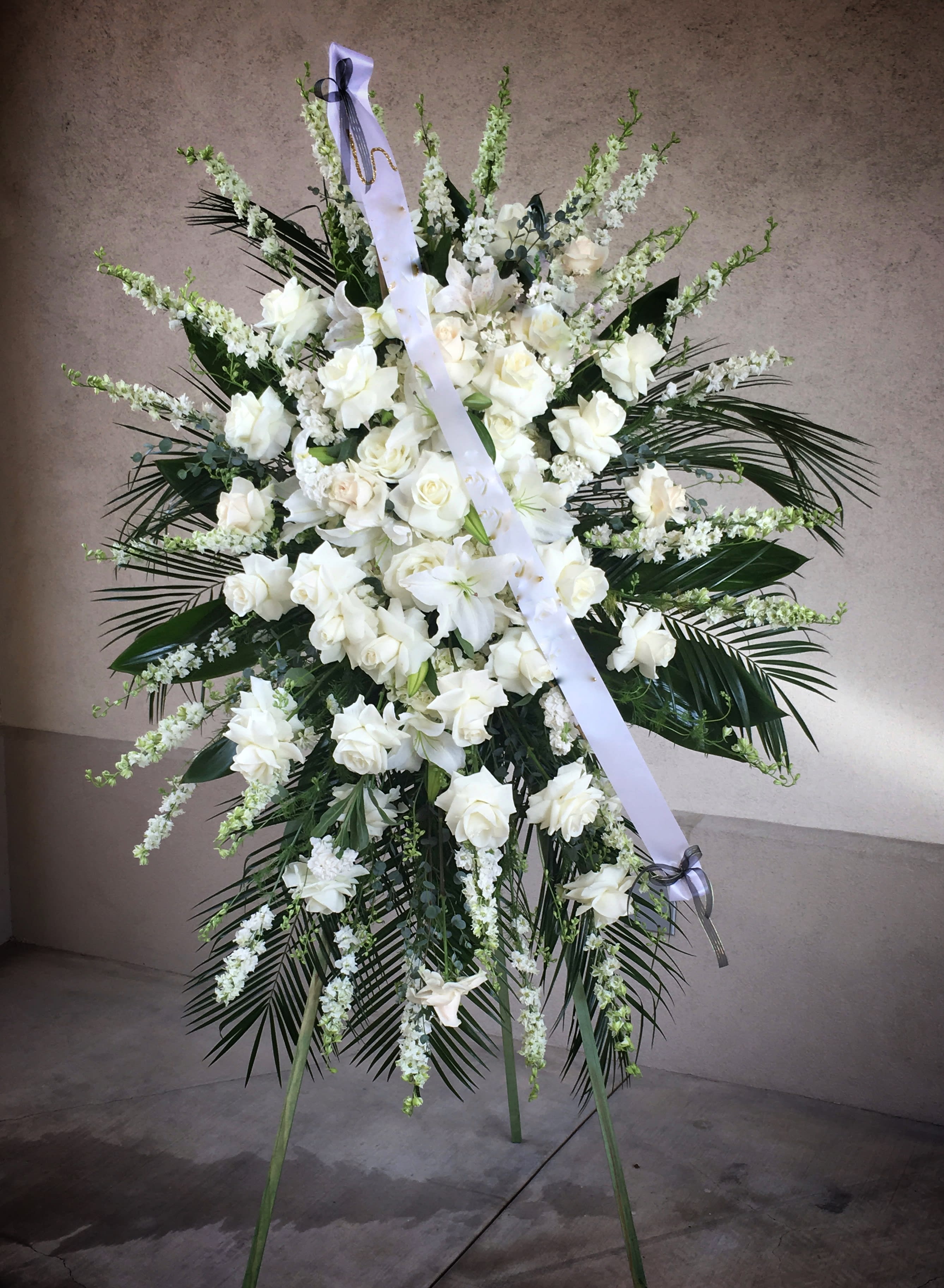 Large white funeral spray on a stand with ribbon
