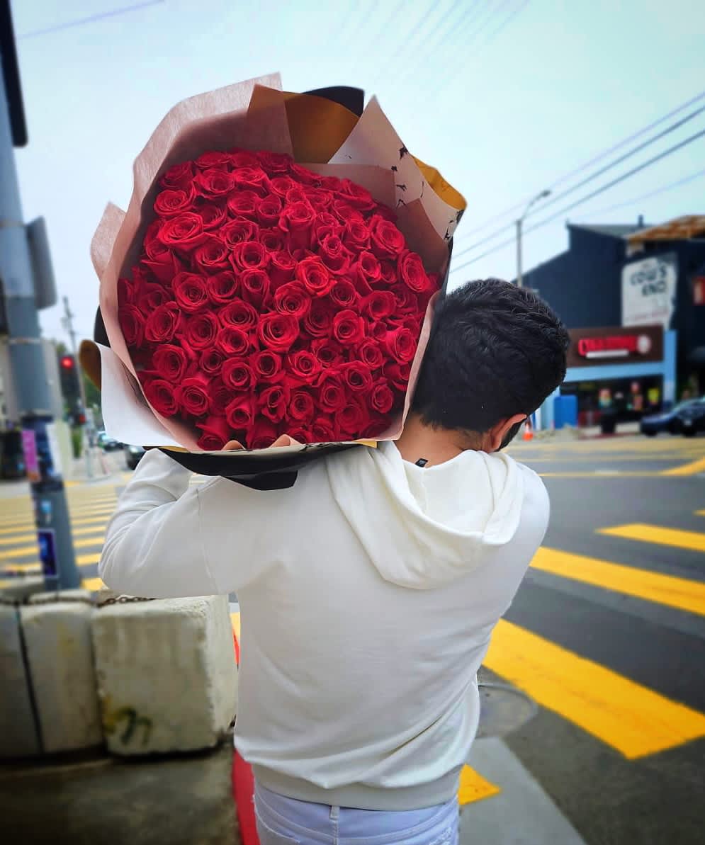 Large armful bouquet of tightly packed red roses wrapped in kraft paper, carried on a person's shoulder