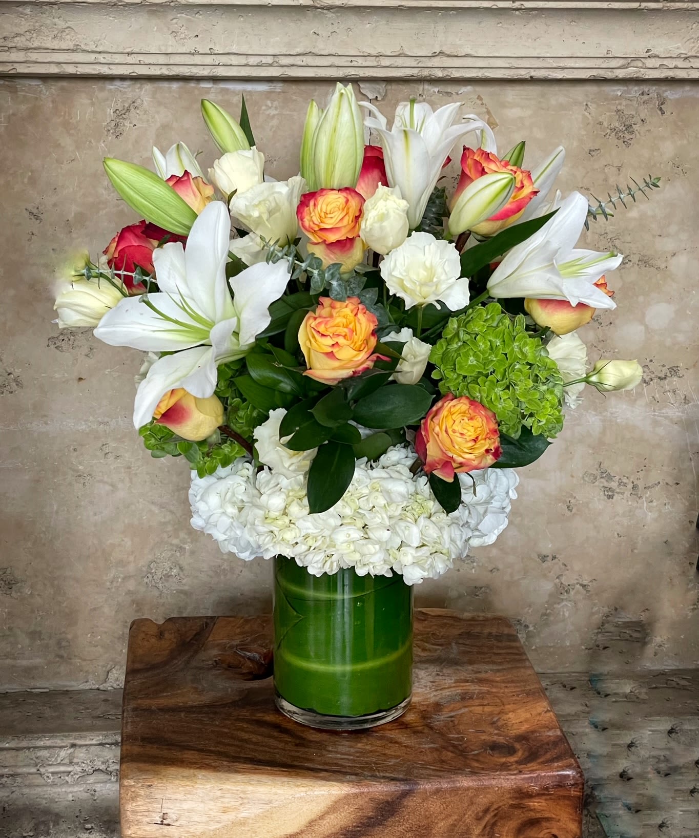 Bouquet of white lilies, roses, and hydrangeas in a green glass vase
