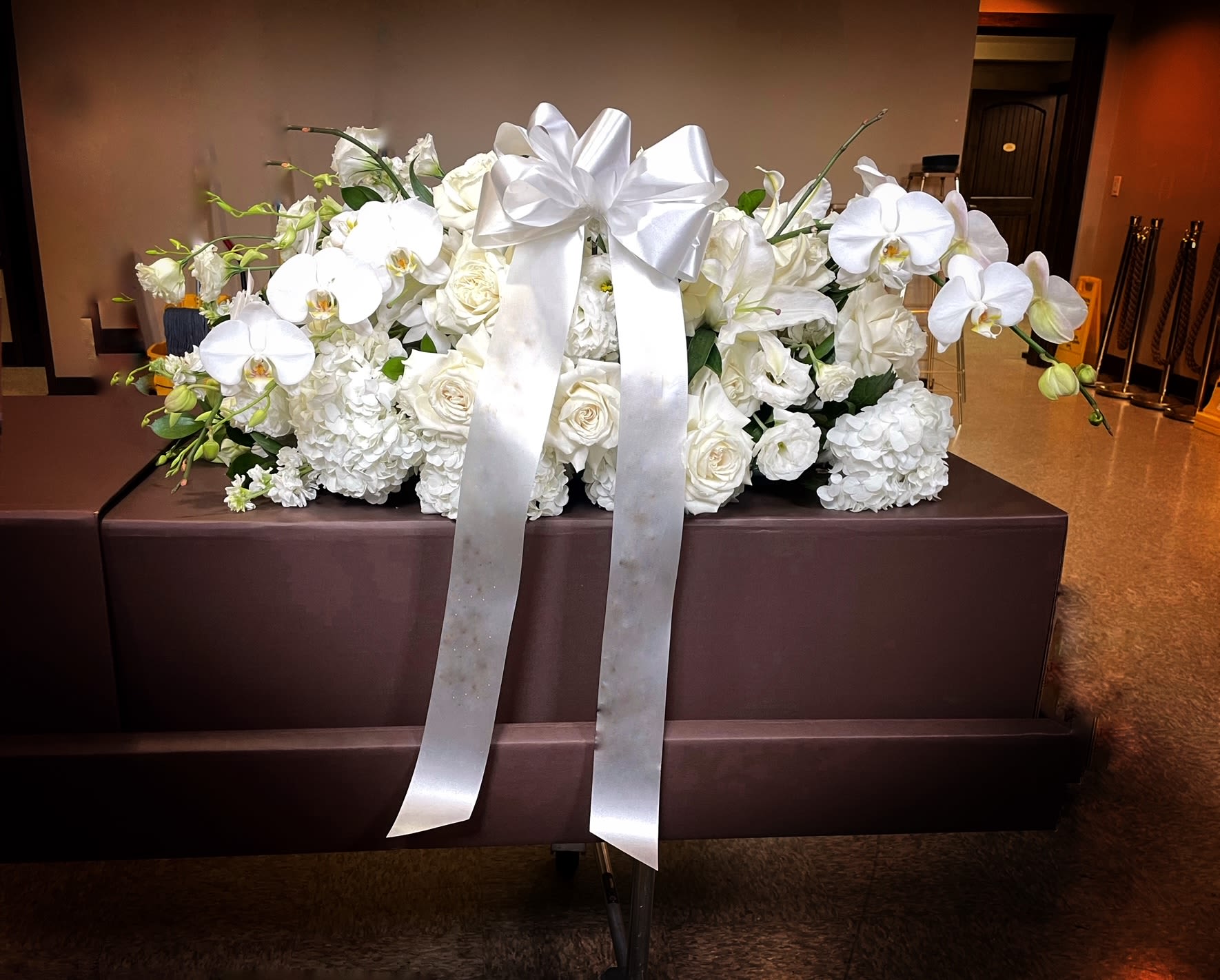 White floral casket spray with orchids, roses, and a large satin bow