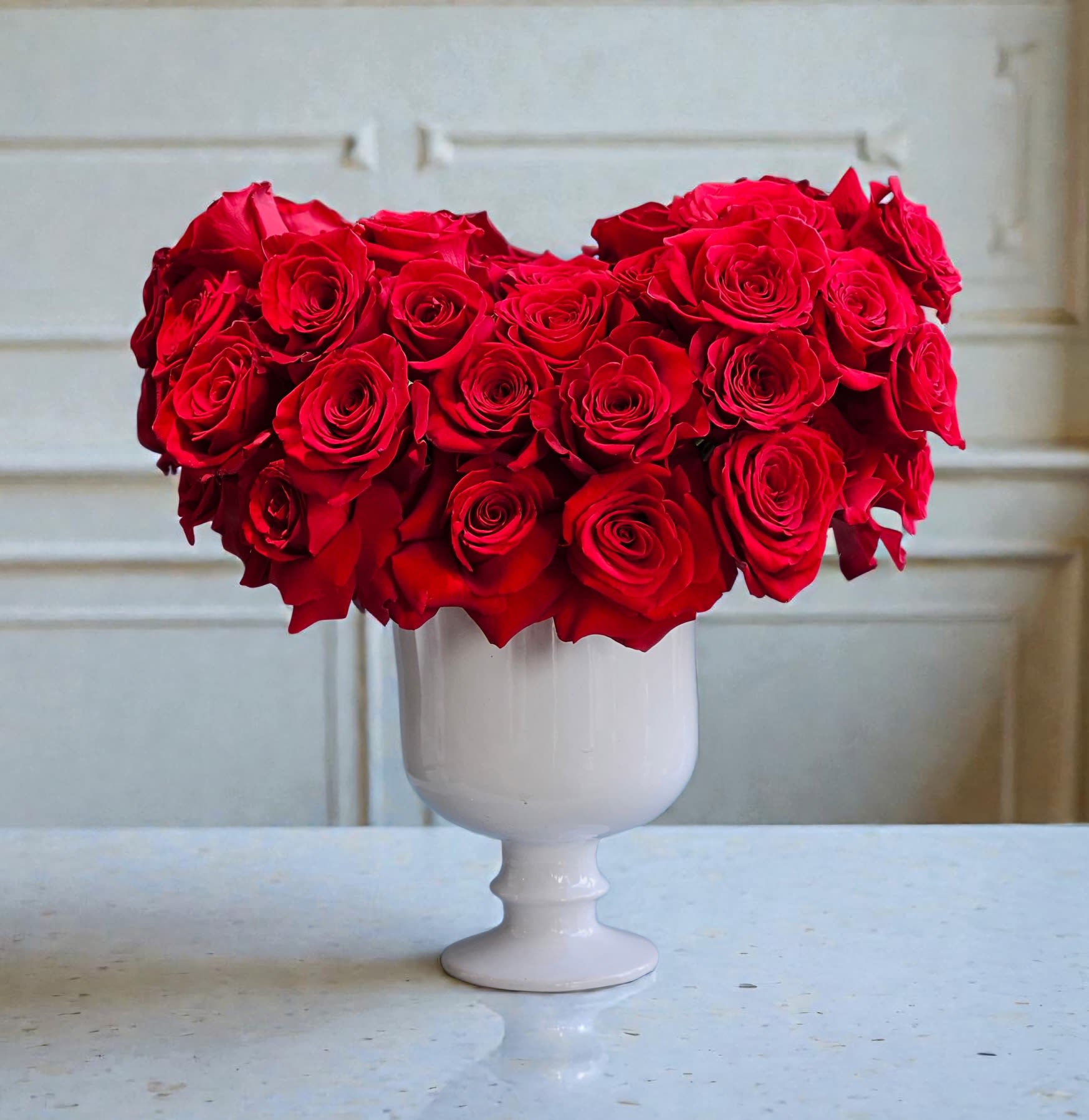 Red roses arranged in a white pedestal vase