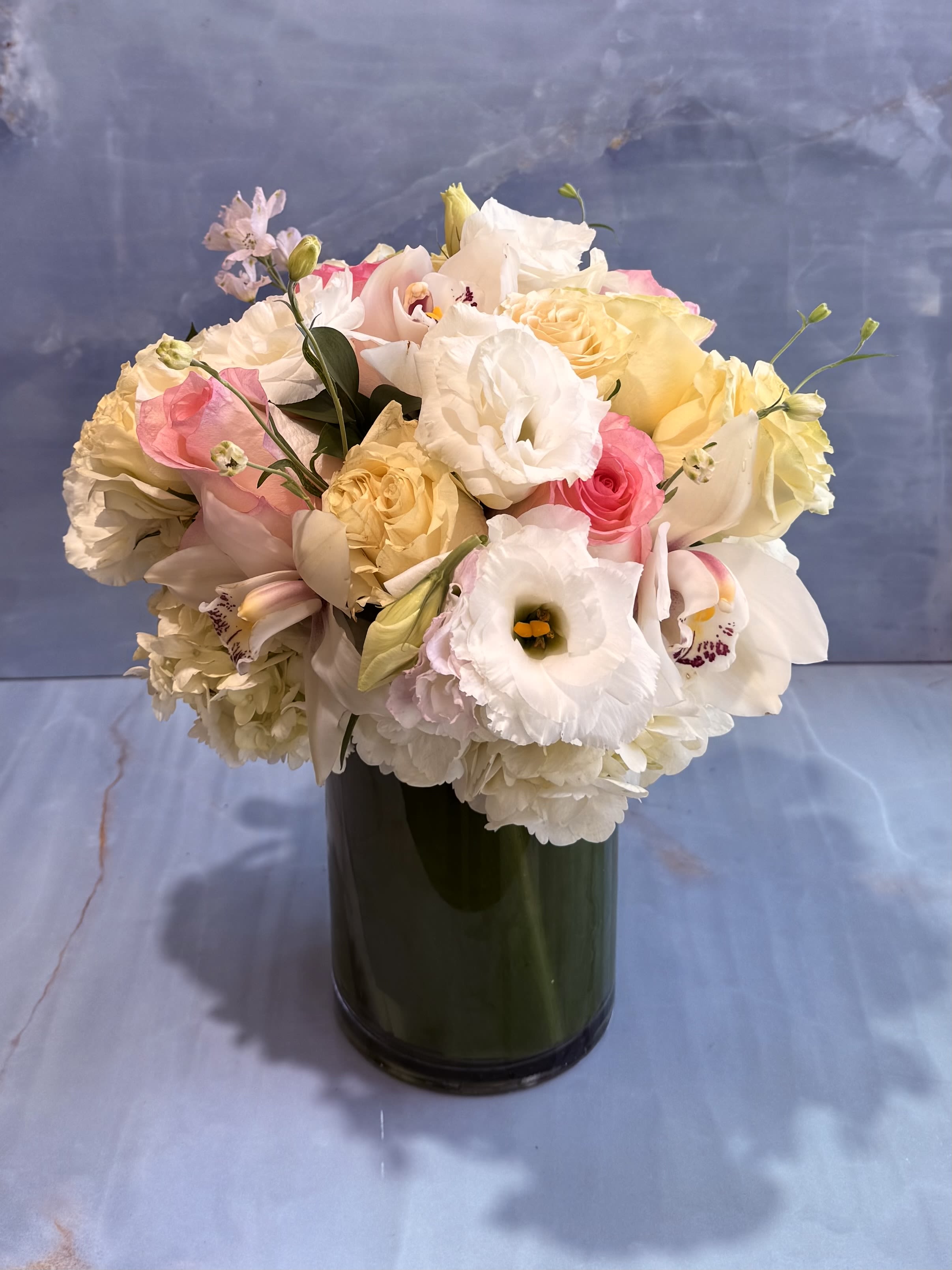 French Linen  - This arrangement feels soft, romantic, and effortlessly elegant. A lush gathering of blush pink roses, creamy ivory roses, white lisianthus, delicate cymbidium orchids, and cloud-like hydrangea creates a design that is both refined and inviting. The gentle palette of blush, champagne, ivory, and soft pink gives the arrangement a fresh garden-inspired feel, white the orchids add a touch of sophistication and luxury. 