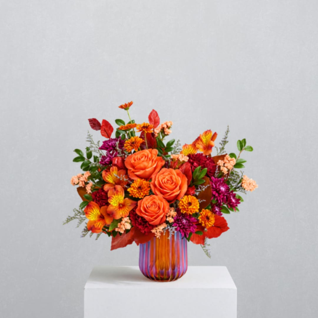 Orange and red mixed bouquet in a striped glass vase