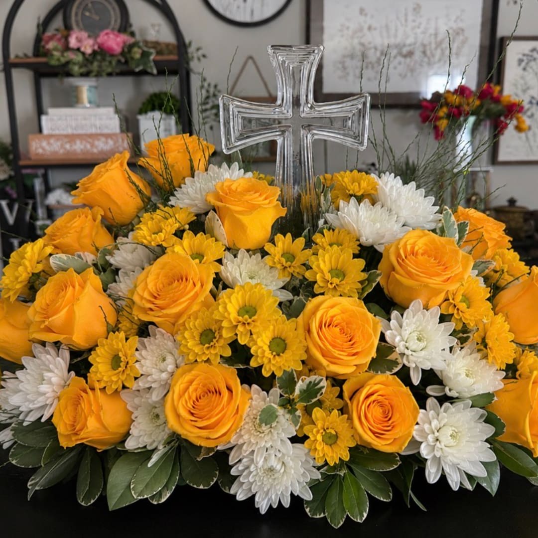 Yellow roses and white chrysanthemums arranged around a clear glass cross