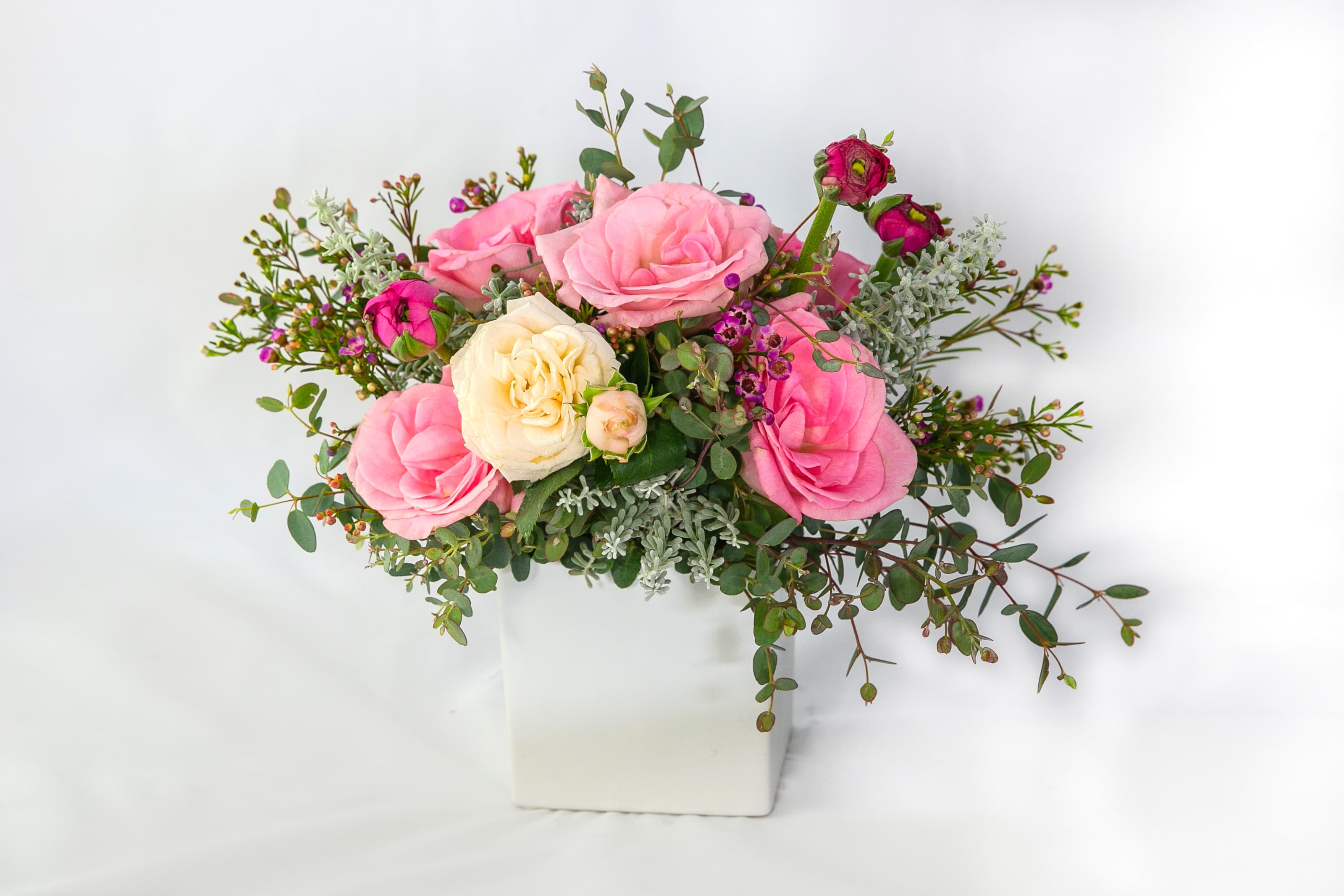 Pink and cream roses arranged in a white square vase