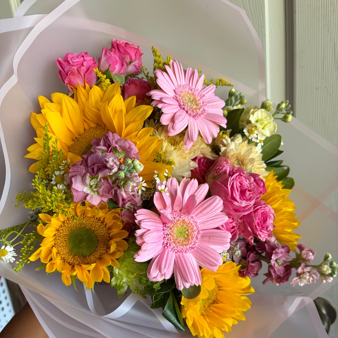 Bouquet of pink gerbera daisies, yellow sunflowers, and pink roses wrapped in white paper
