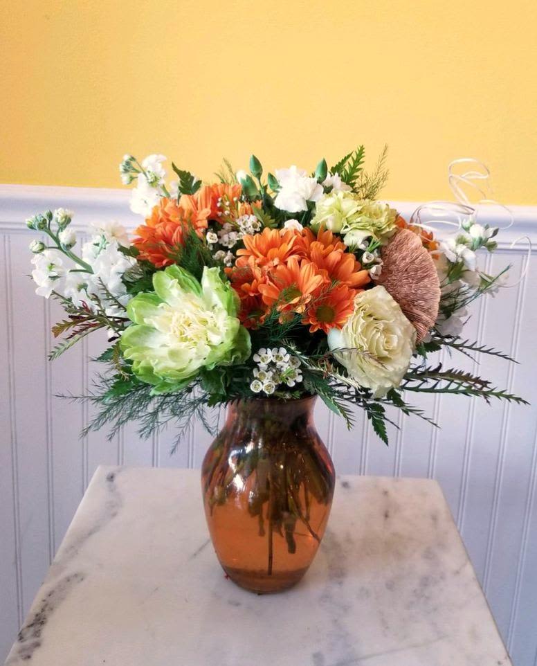 Orange and white flower arrangement in an amber glass vase