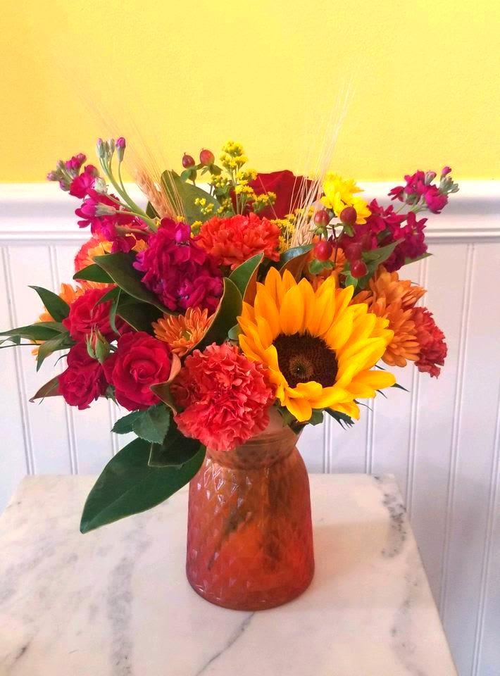 Colorful mixed bouquet in an amber glass vase with a sunflower and roses