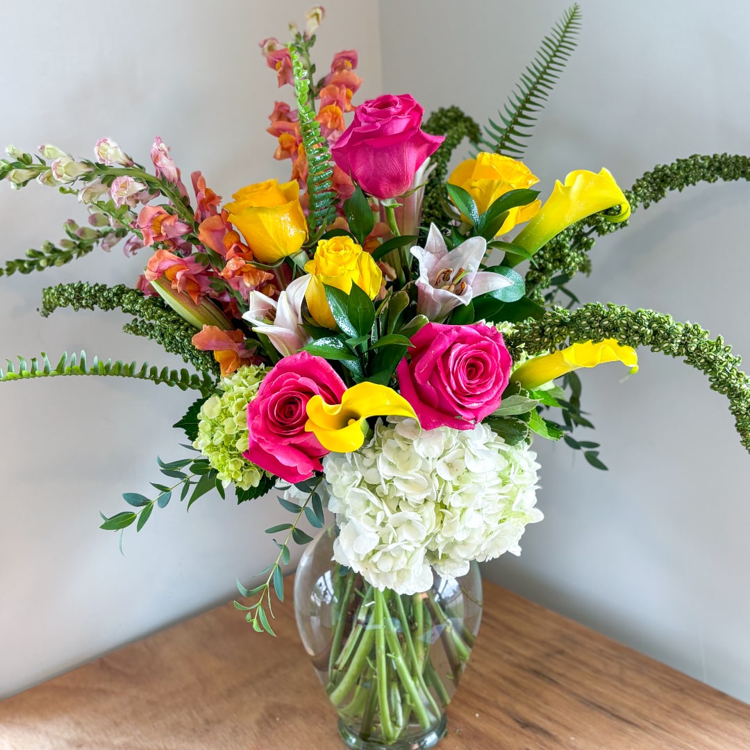 Bright mixed bouquet with pink roses, yellow calla lilies, and white hydrangeas in a glass vase