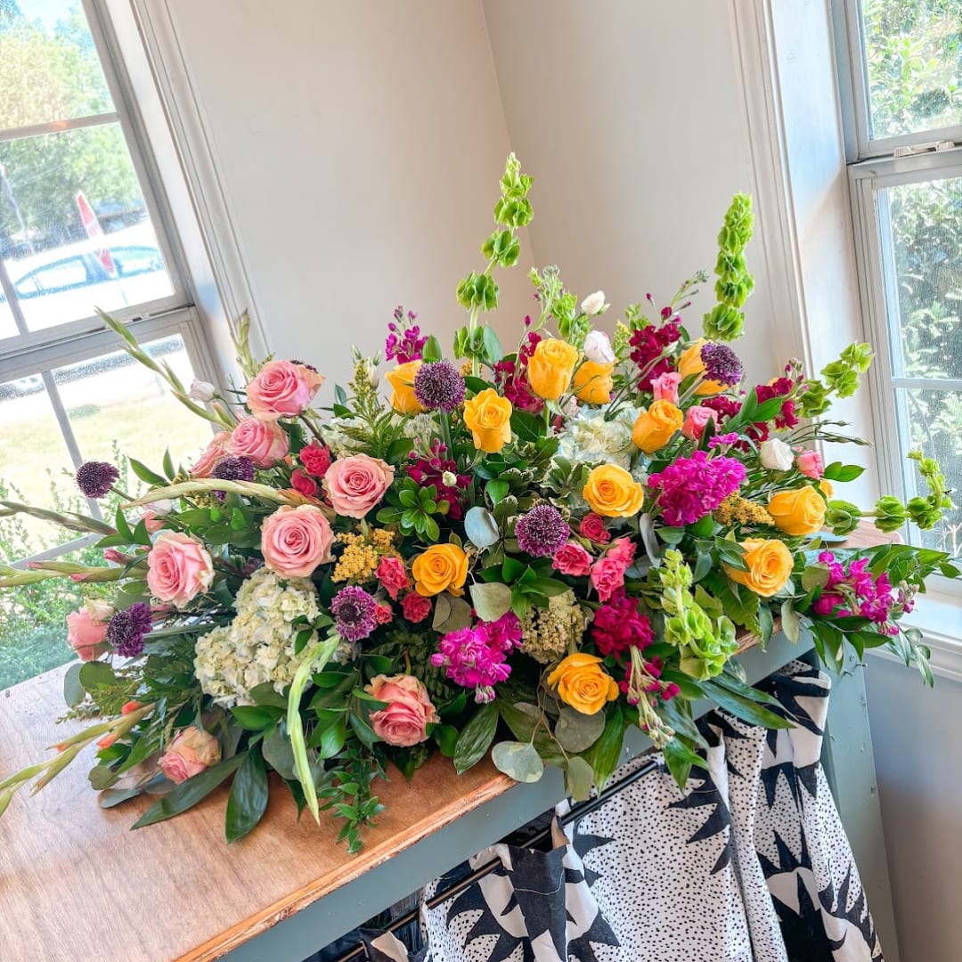 Large mixed floral arrangement with pink and yellow roses in a low container