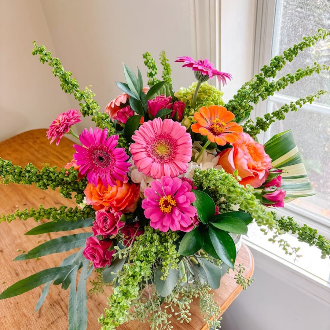 Bright mixed bouquet with pink gerberas, orange roses, and green filler in a vase