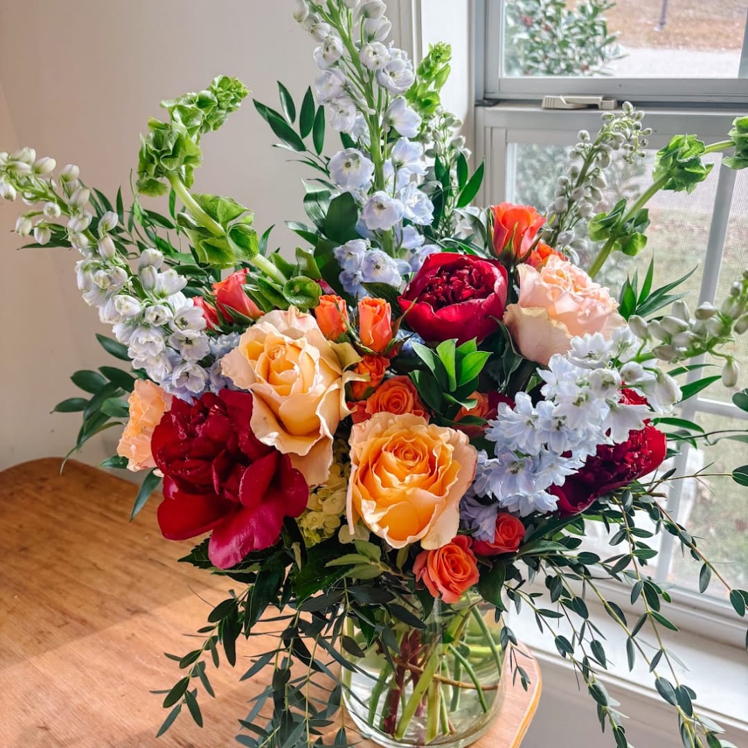 Mixed bouquet of roses, peonies, and blue flowers in a glass vase