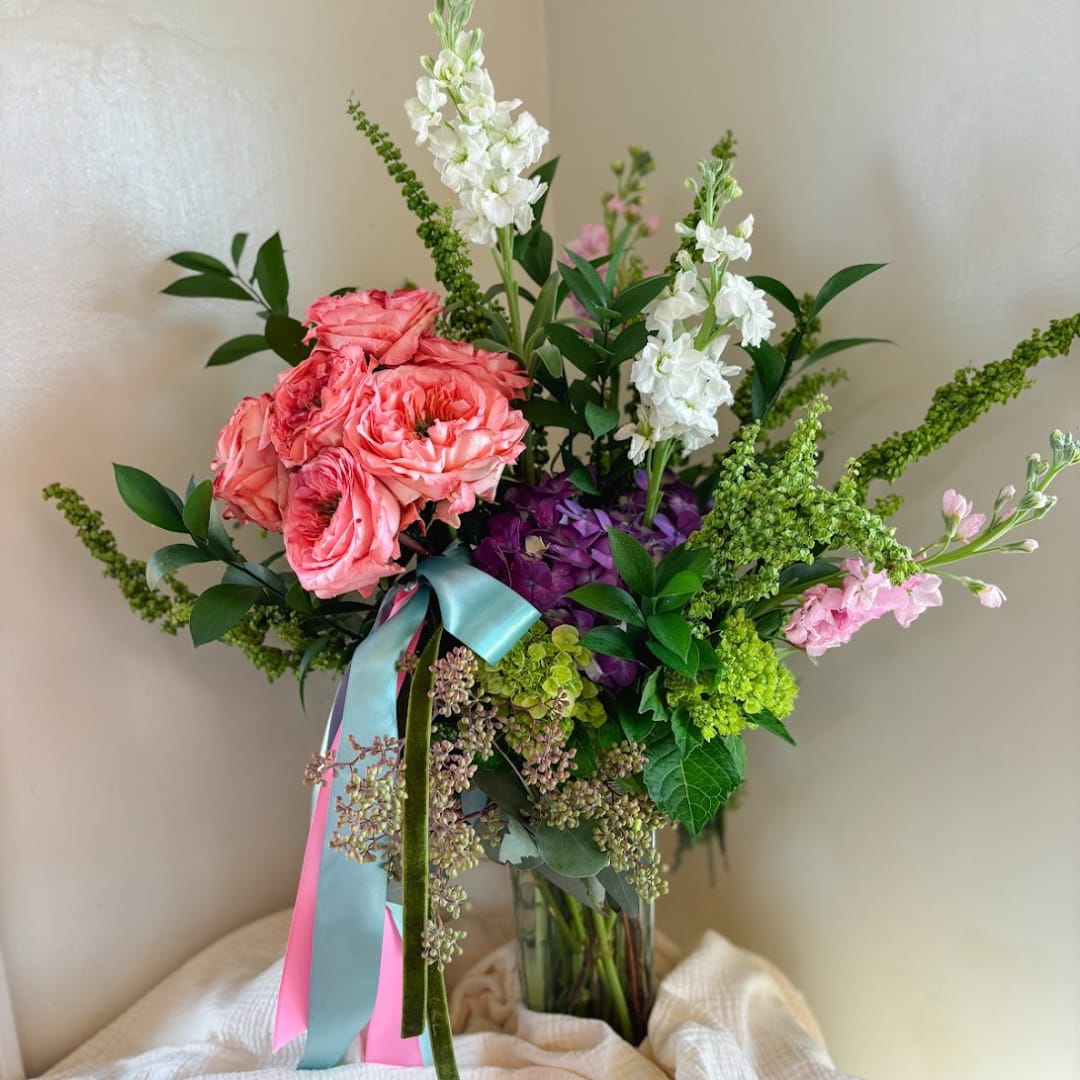 Pink and white flowers arranged in a clear glass vase with a ribbon