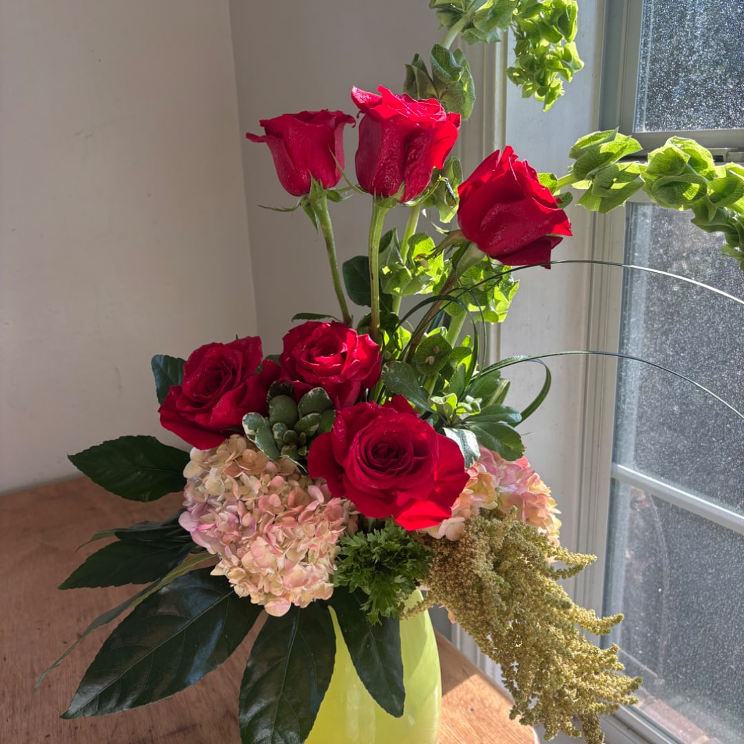 Red roses and pale hydrangeas in a lime-green vase by a window