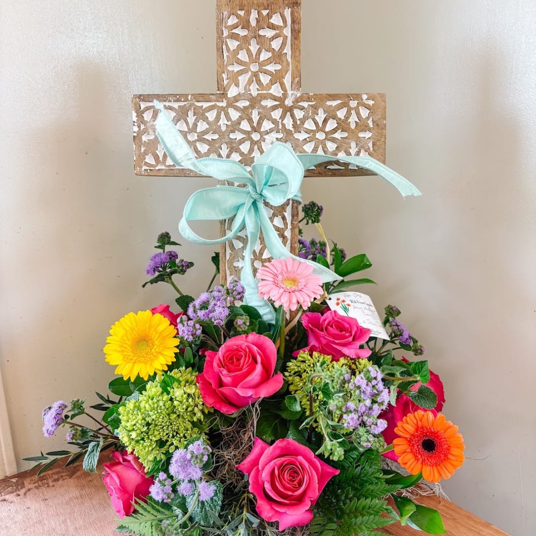Colorful flower arrangement in front of a decorative wooden cross with a blue ribbon