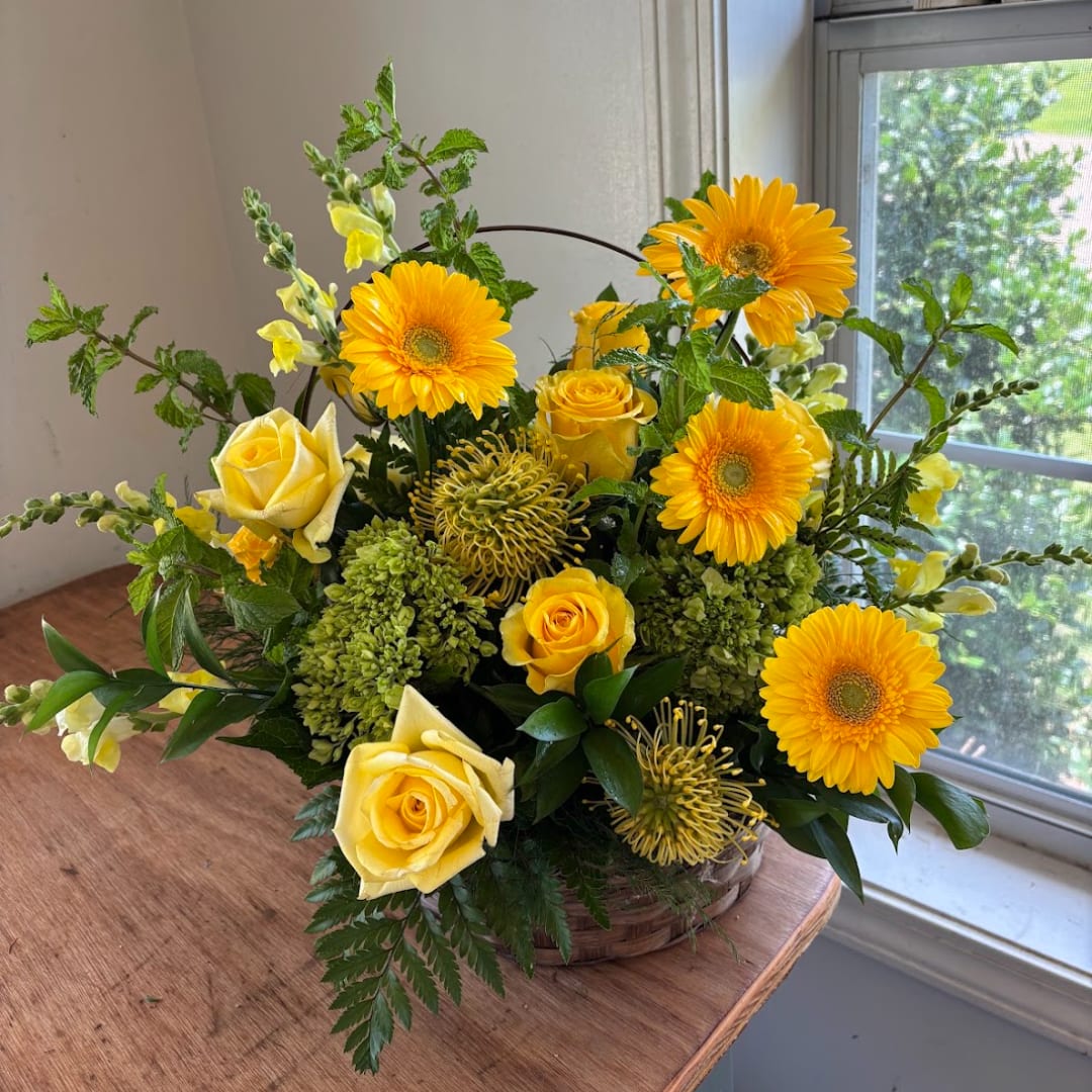 Yellow roses and gerbera daisies in a low basket arrangement