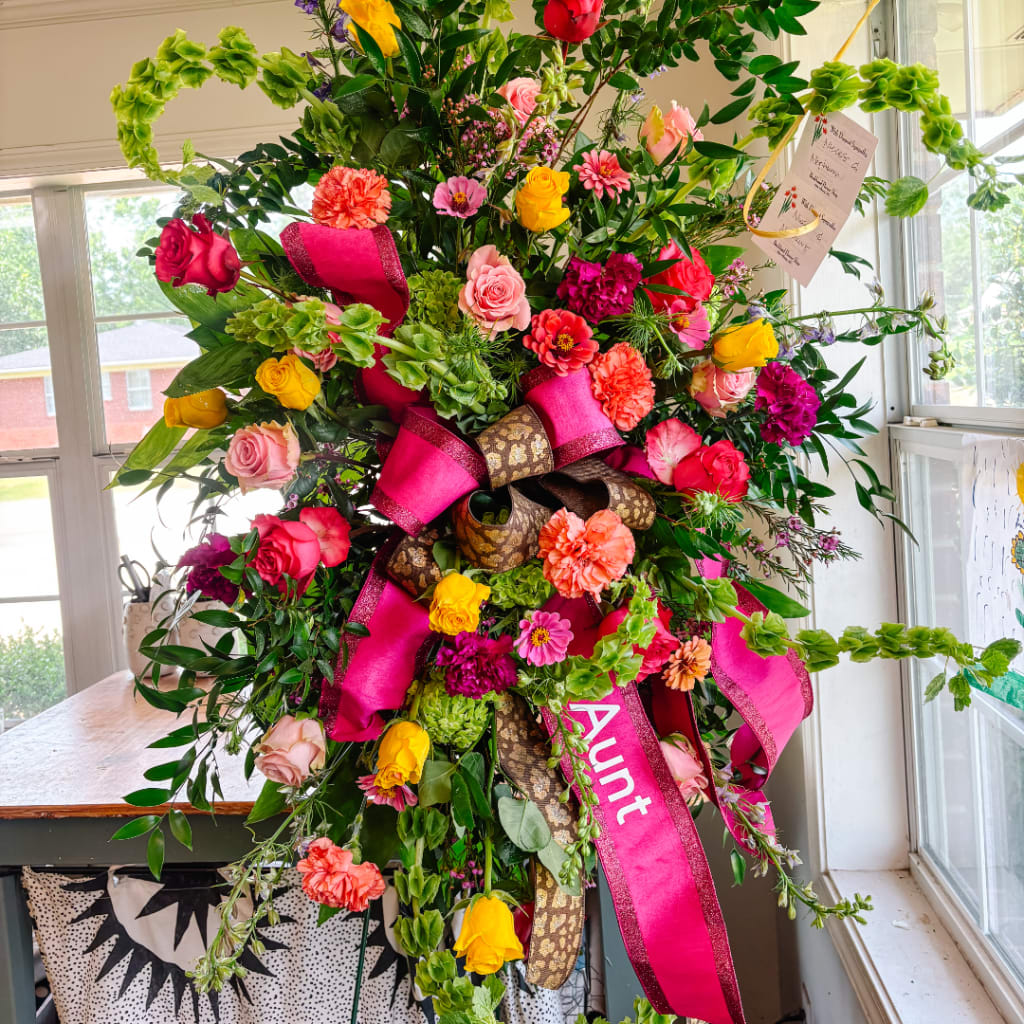 Large floral standing spray with bright mixed flowers and pink ribbons