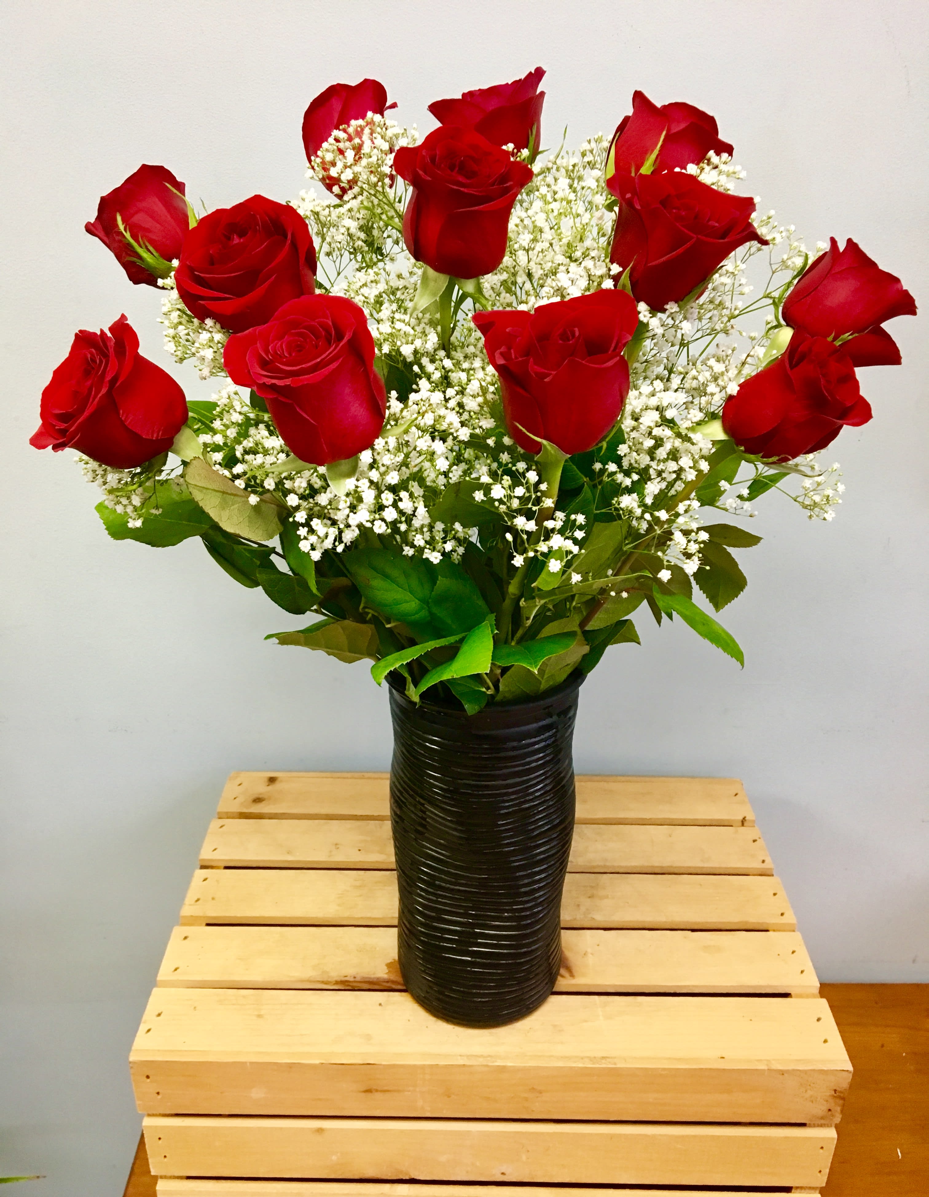 Red roses arranged in a black vase with white filler flowers