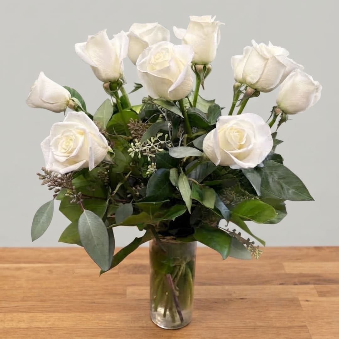 White roses arranged in a clear glass vase with greenery